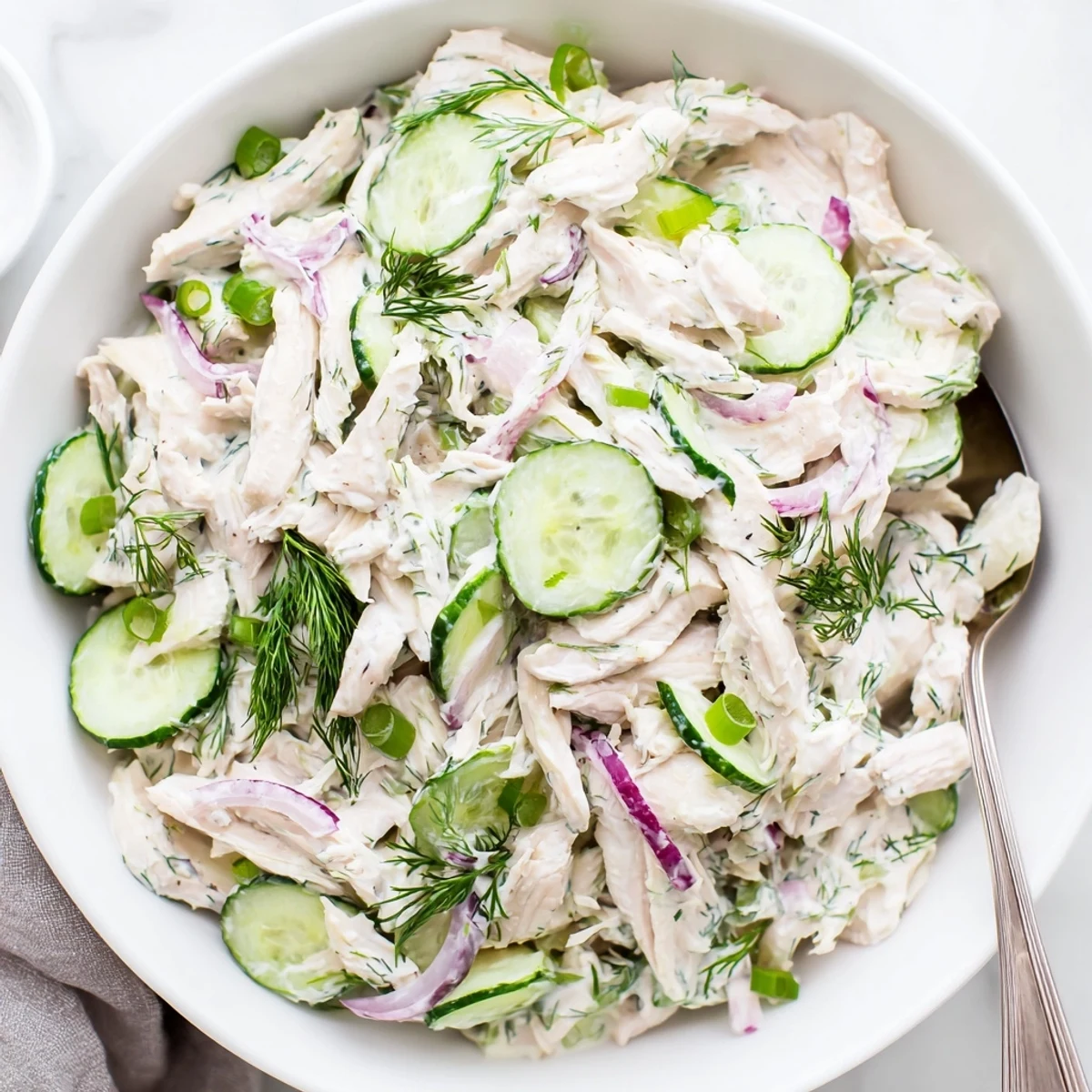 Chilled Creamy Cucumber Chicken Salad in a white bowl, garnished with fresh dill and green onions.