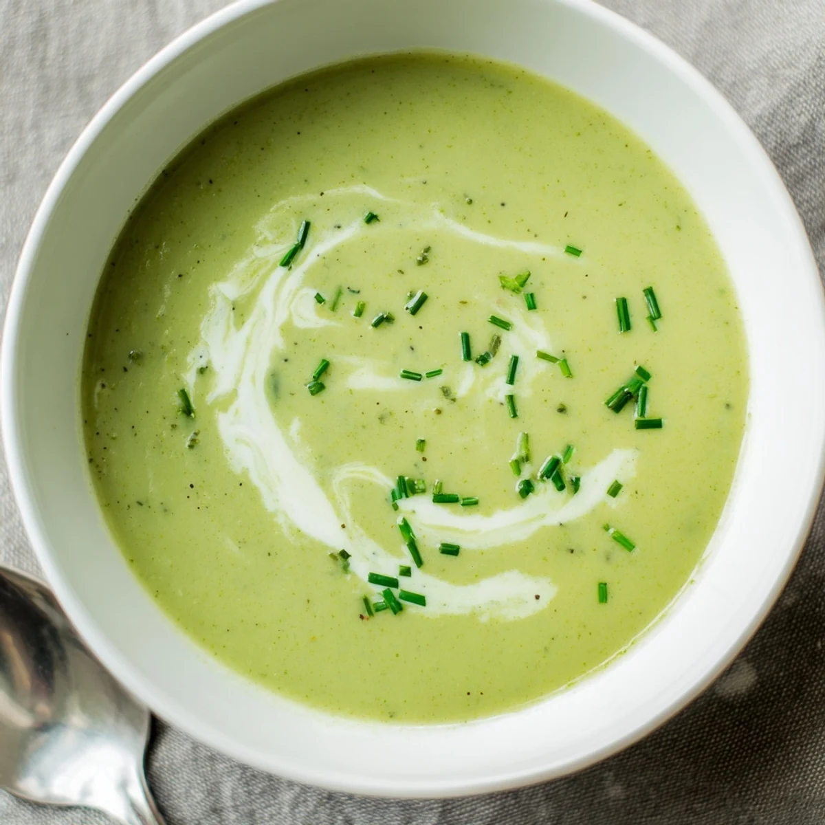 A warm bowl of creamy broccoli soup, garnished with a swirl of cream and fresh chives, served with rustic bread.