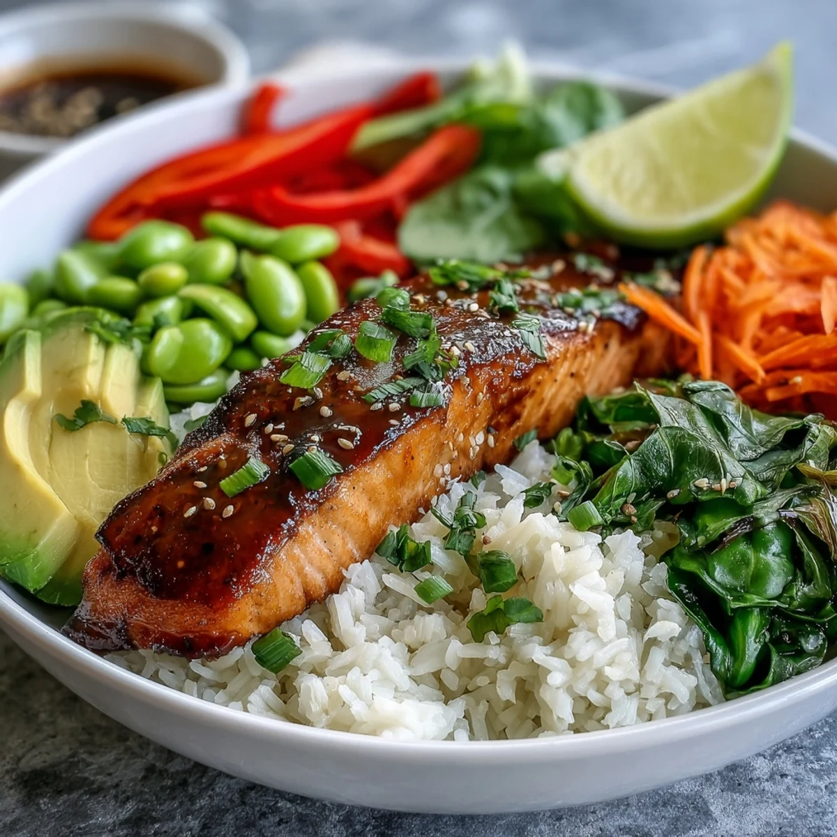 Golden seared salmon fillet glazing in a bowl with crisp veggies and rice, served with lime wedges.