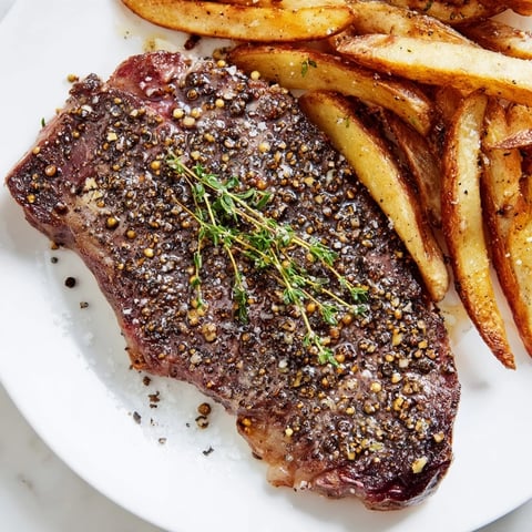 Sizzling Classic Peppercorn Ribeye with golden, crispy fries, a delicious steakhouse dinner ready.