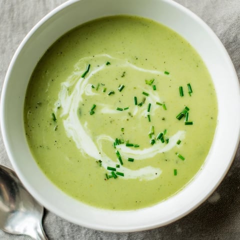 A warm bowl of creamy broccoli soup, garnished with a swirl of cream and fresh chives, served with rustic bread.