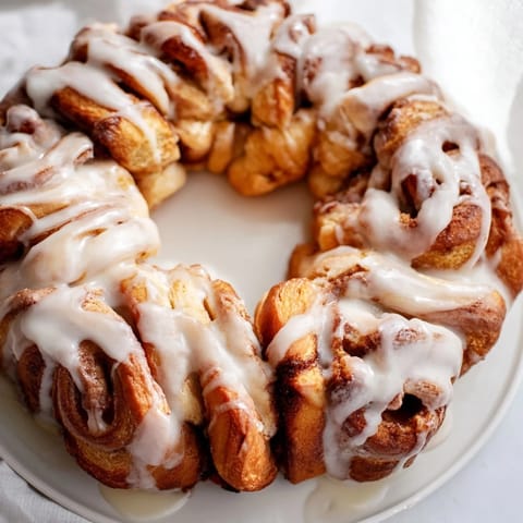 A close-up of a warm, inviting cinnamon roll wreath with a glistening vanilla glaze, ready to eat.