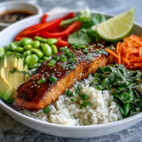 Golden seared salmon fillet glazing in a bowl with crisp veggies and rice, served with lime wedges.