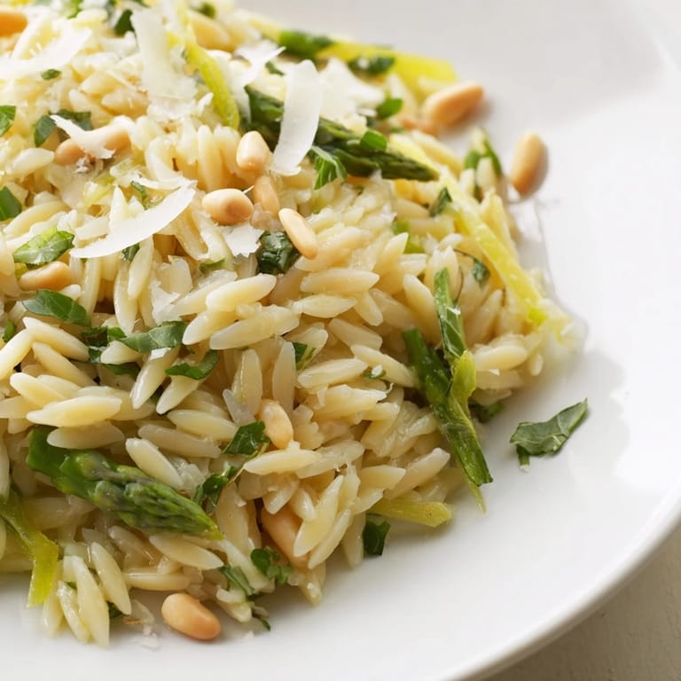 Shaved asparagus and orzo salad with lemon dressing and Parmesan, garnished with fresh parsley, served alongside grilled chicken on a plate.